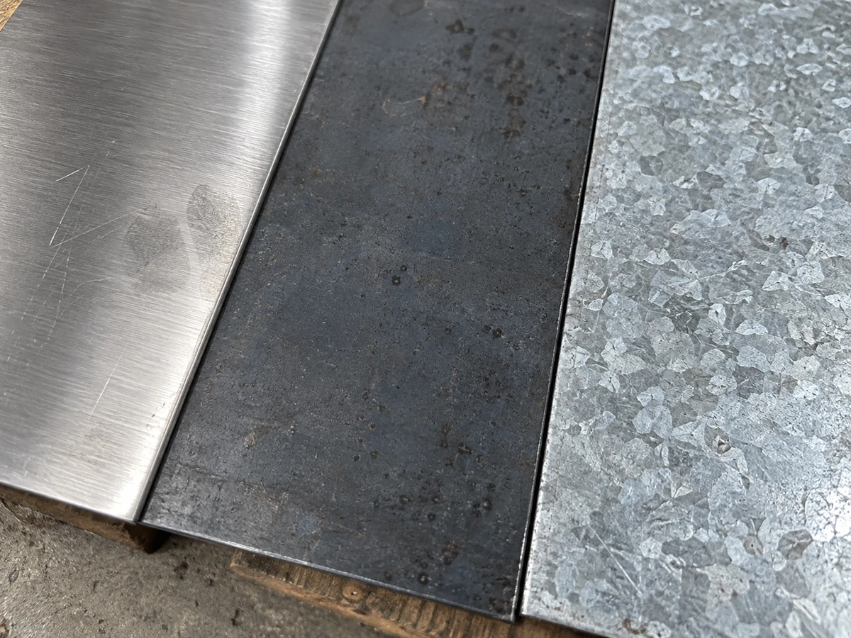 Samples of stainless, carbon and galvanized steel laid side by side, each surface distinct.