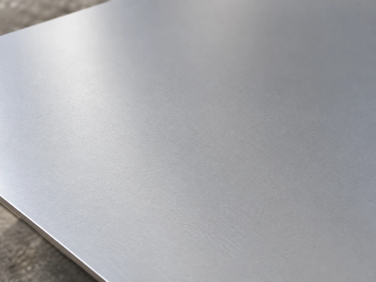 A 2B stainless steel sheet surface, matte and even, reflecting the light softly.