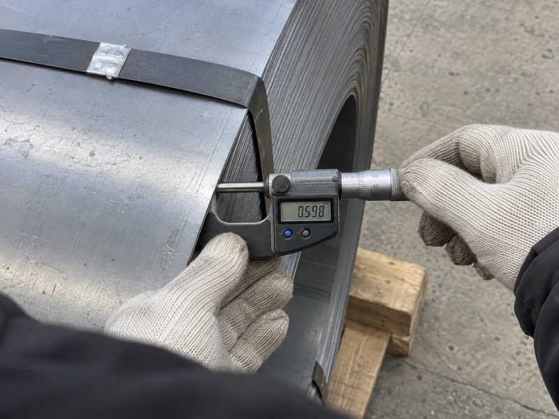 An SPCC coil being measured for thickness before shipment, the reading visible.
